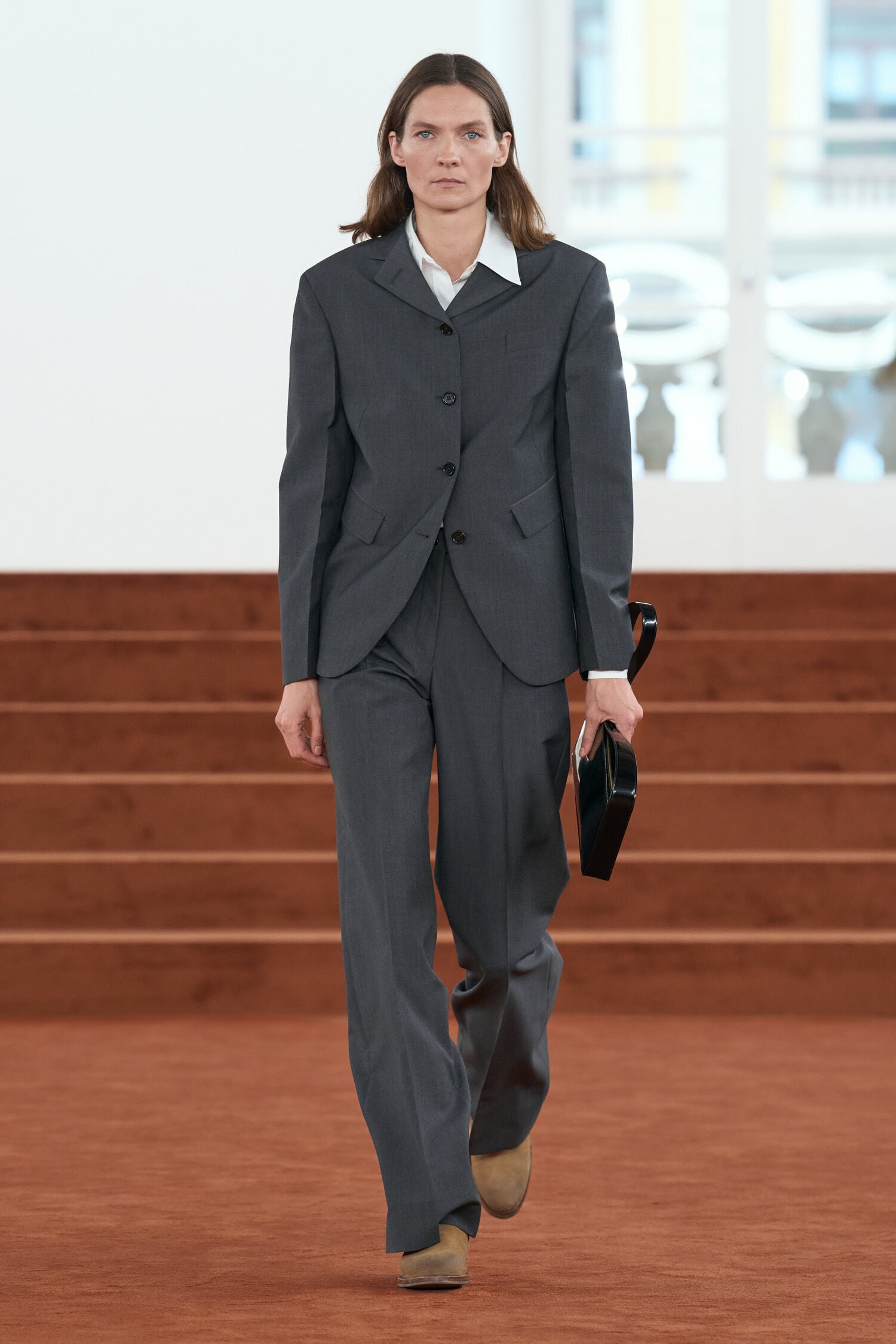 A model wearing charcoal tailoring on the rust-coloured runway at the Jil Sander Autumn/Winter 2026 show in Milan
