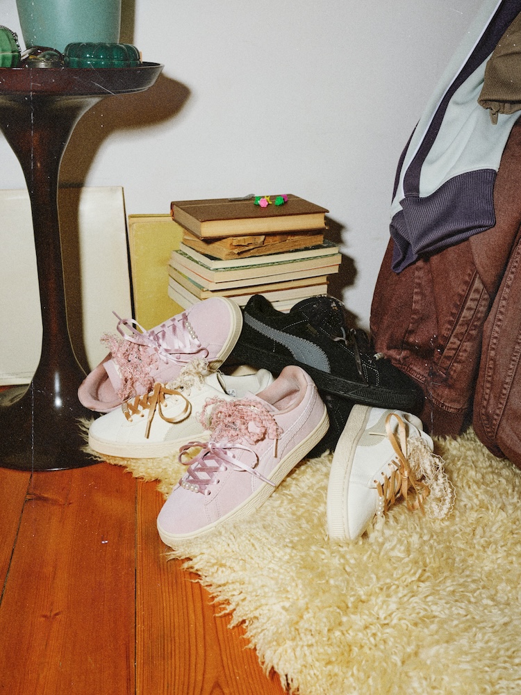 PUMA Suede Bloom trainers in Powder Pink, Black and Vintage Cream arranged beside books and clothing.