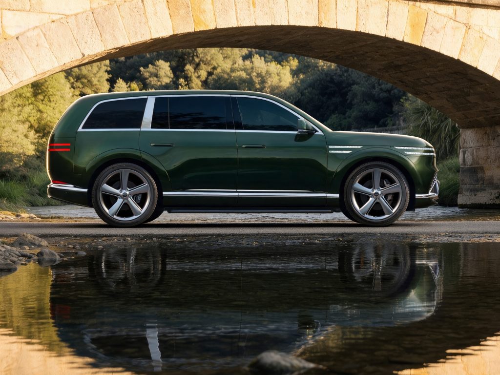 Green Genesis GV90 in side profile beneath a stone arch with its reflection visible in water.