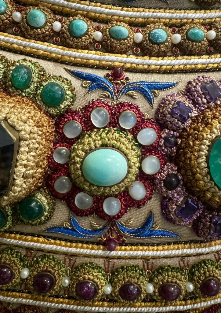 Gemstone rosette surrounded by smaller stones and intricate embroidery in The Vase.