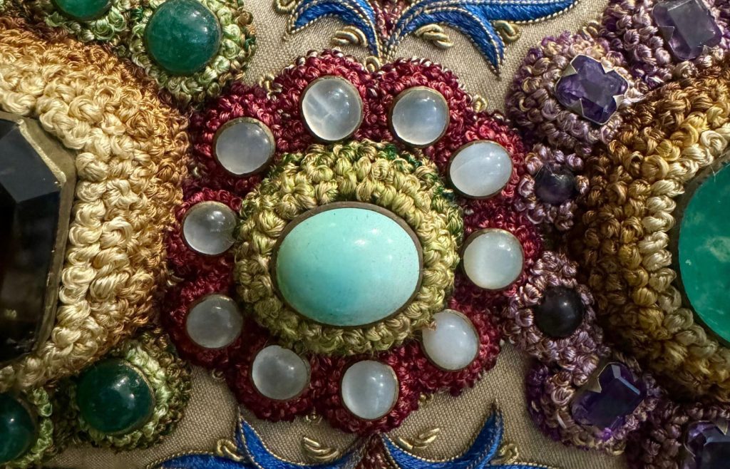 Close view of a gemstone rosette, cabochons and embroidered floral details in The Vase.