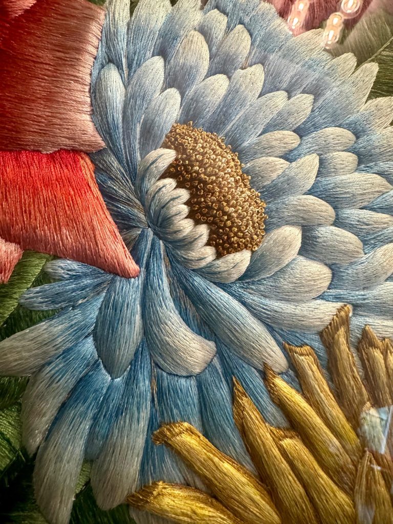 Close view of pale blue silk petals beside red and yellow flowers in The Vase.