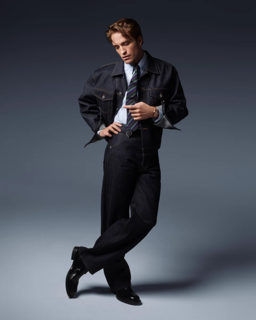 Full-length portrait of Robert Pattinson in dark denim wearing the pink-gold Jaeger-LeCoultre Master Control Chronometre Perpetual Calendar.