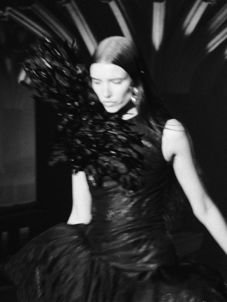 Full-length silhouette showcasing architectural drama of feathered and laced ensemble