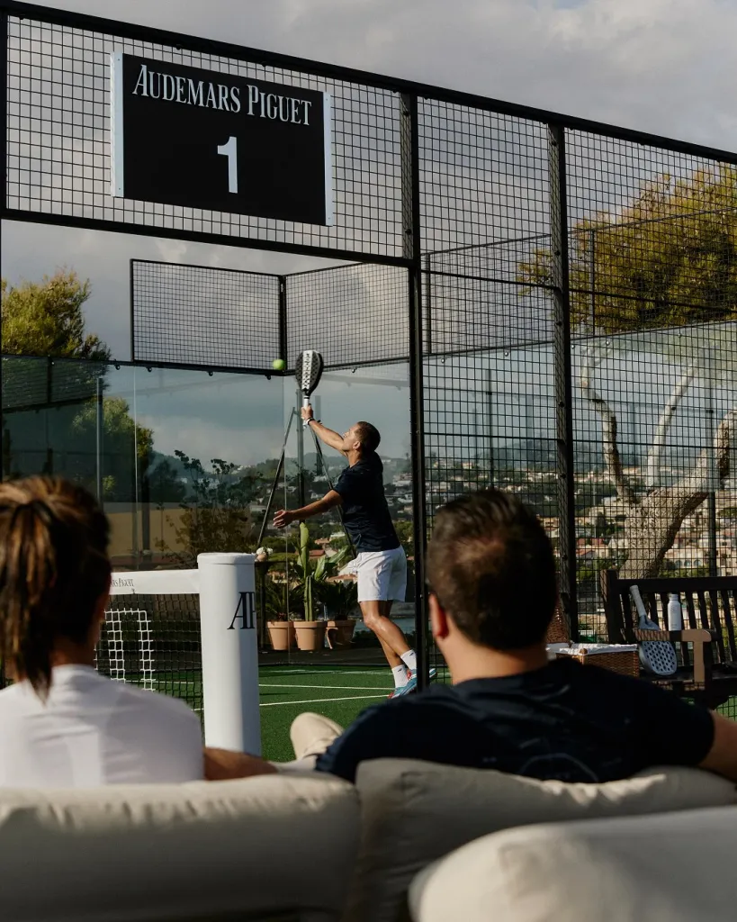 Close-up of players executing precise padel shot with Mediterranean coastline beyond
