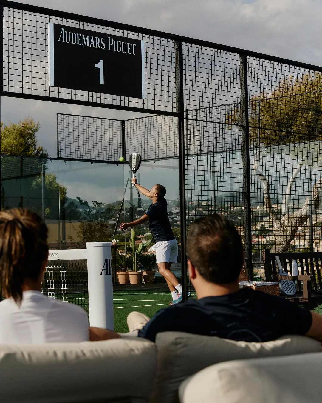 Close-up of players executing precise padel shot with Mediterranean coastline beyond
