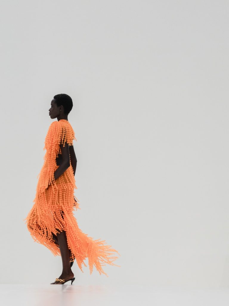 Profile view of sculptural coral dress with contemporary proportions