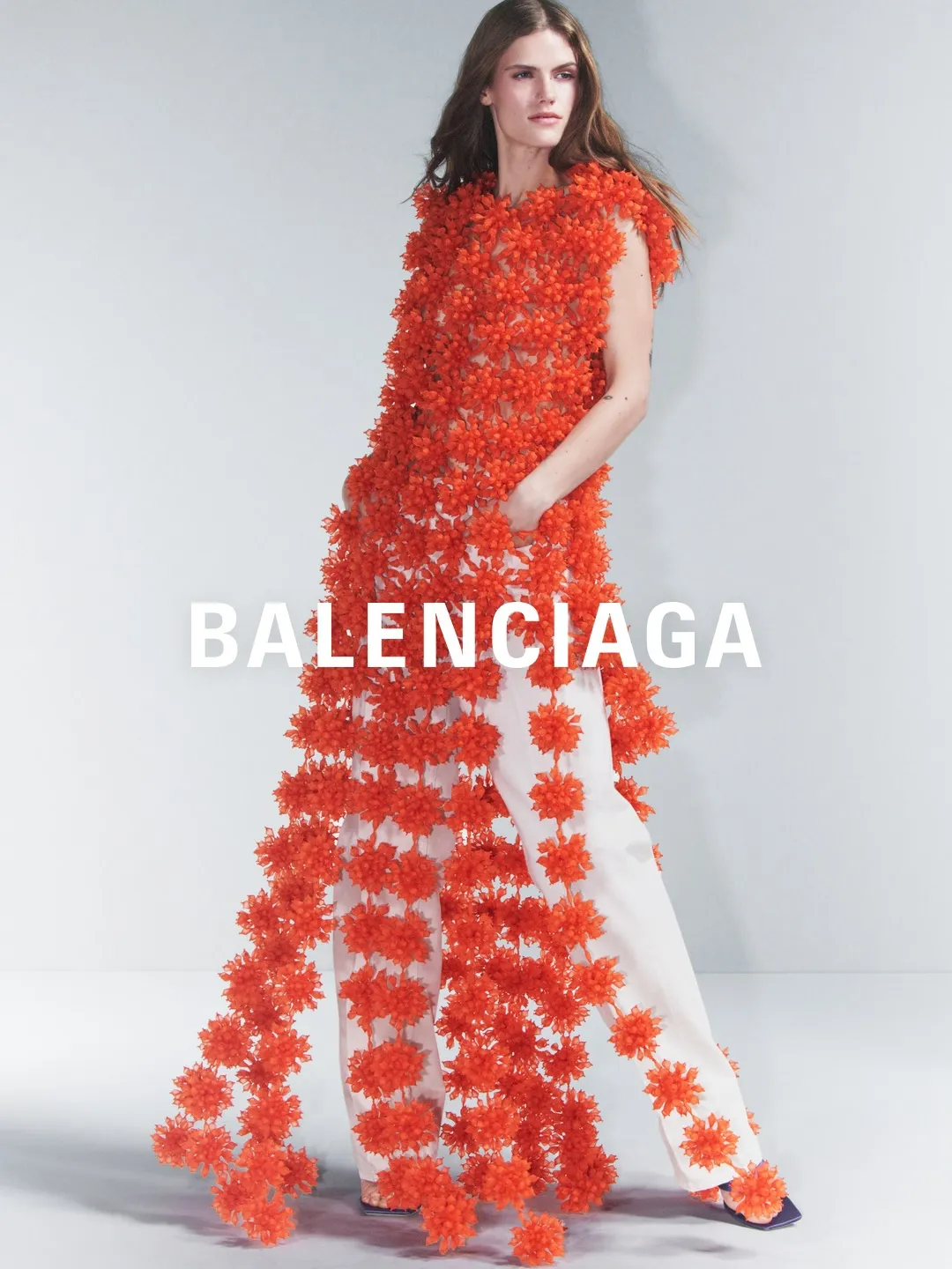 Model wearing saturated coral red tailored pieces with precise, minimalist accessories