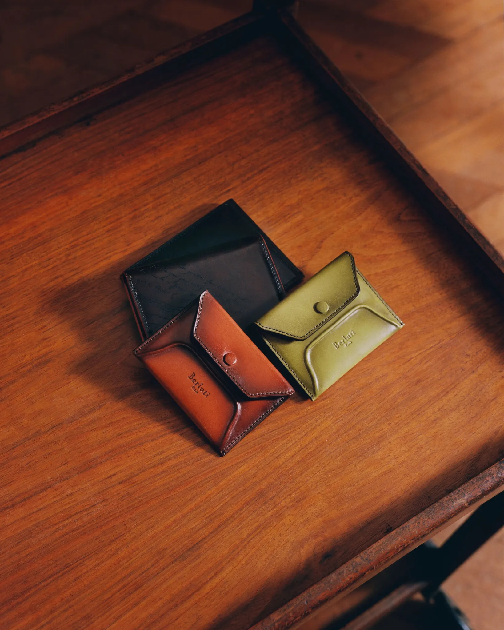 Berluti patinated leather card holder in deep, shifting tones, displaying subtle creases and refined folds reminiscent of a treasured envelope
