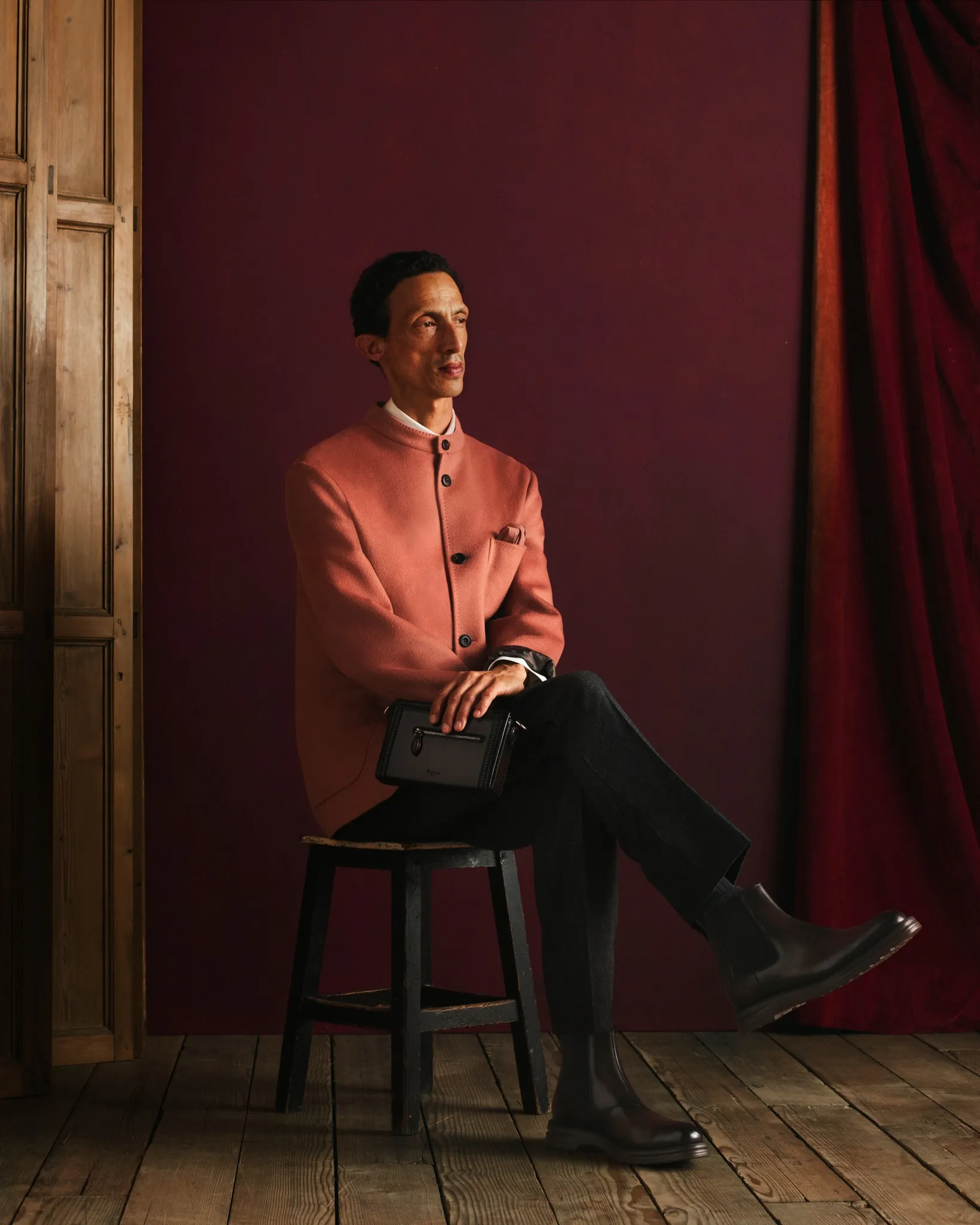 Berluti model wearing rose and grey toned tailoring with deep brown and white contrasting elements, holding the Un Jour de Poche bag, demonstrating ethereal silhouettes caught between light and shadow