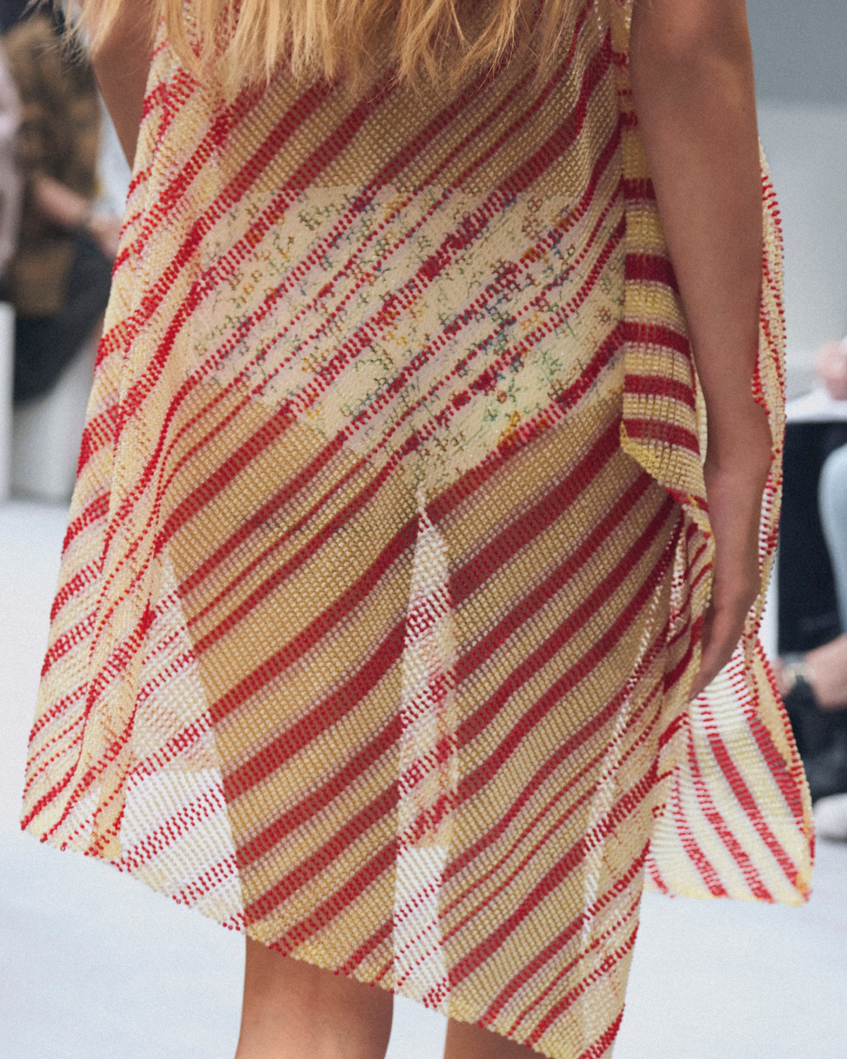 Close detail of intricately woven glass bead panels showing the knitwear-like construction and dynamic interplay of light through the transparent material