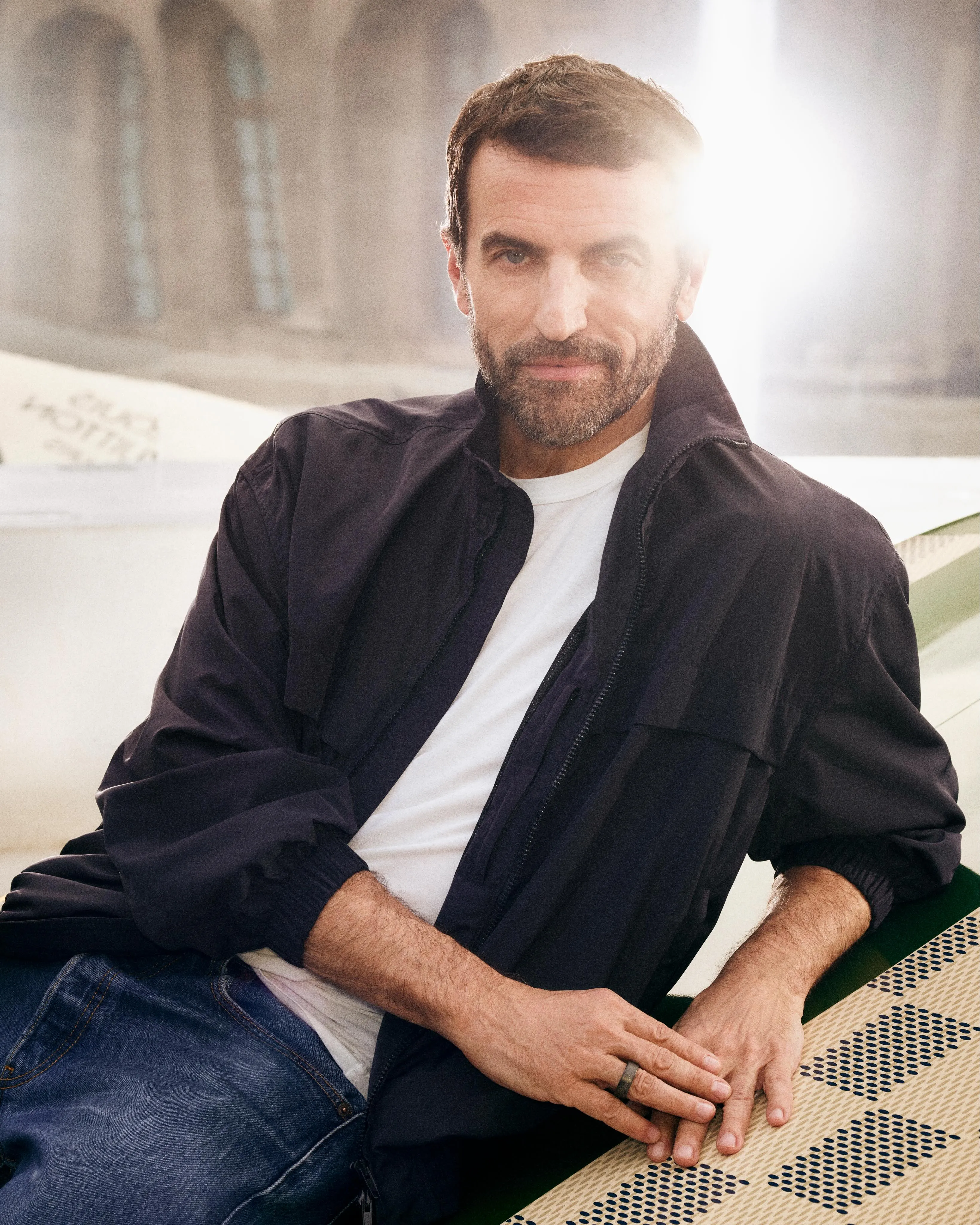 Nicolas Ghesquière stands in portrait at the Cour Carrée du Louvre alongside model Ella Dalton, concept vehicles floating behind them framed by Renaissance architecture
