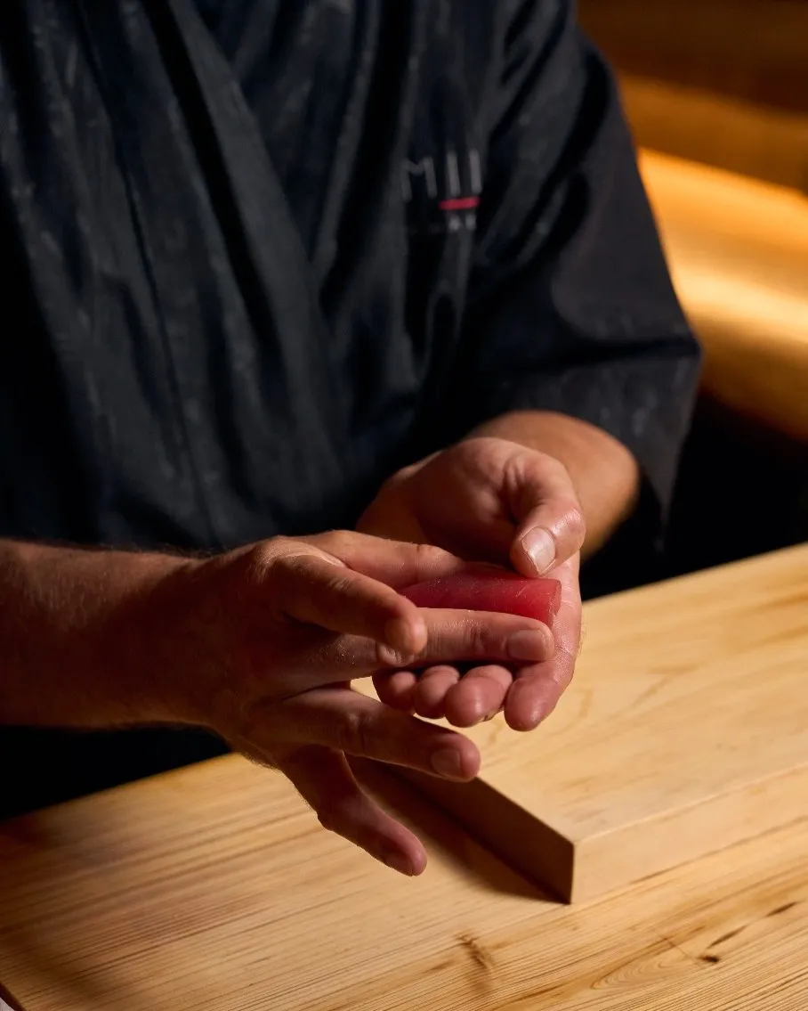 Chef preparing fresh nigiri sushi with precision knife work at MILA Omakase counter