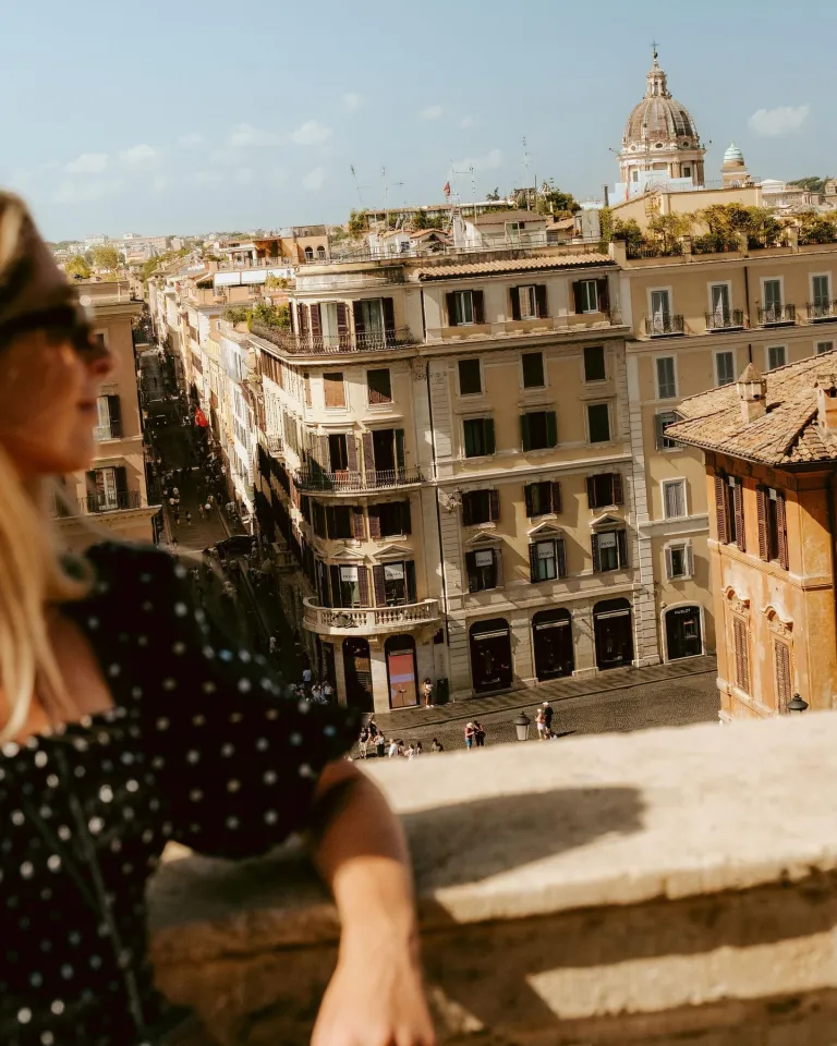 Aerial view of Rome's terracotta rooftops and historic architecture spread across the cityscape beneath clear Italian skies