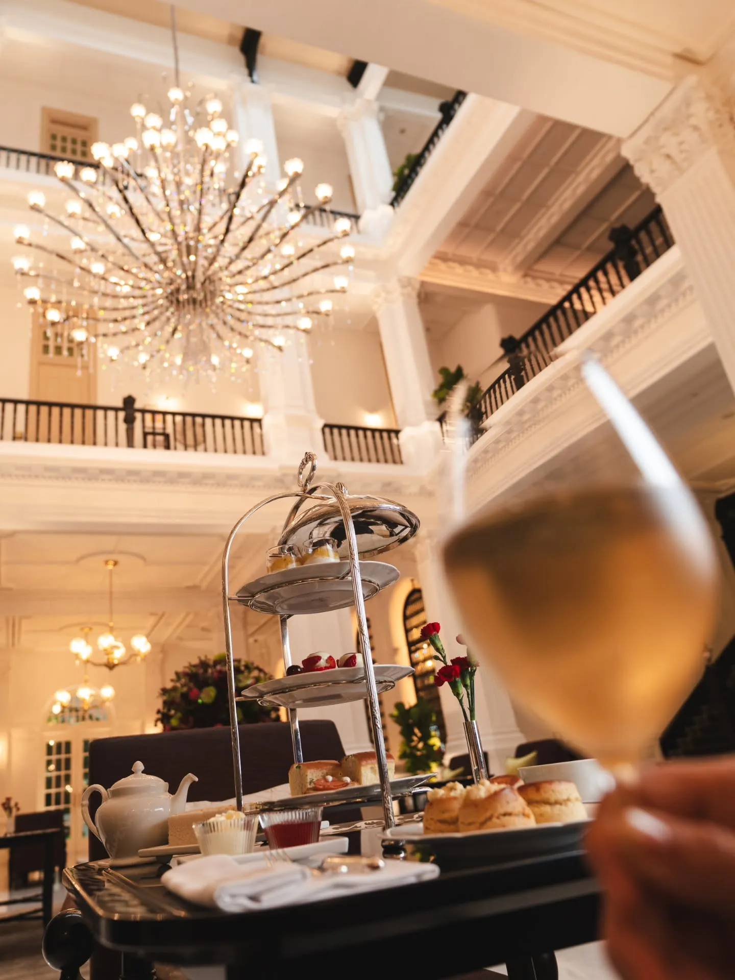 Elegantly presented Champagne Afternoon Tea spread at Raffles Hotel Singapore's Grand Lobby, featuring tiered service of finger sandwiches, scones and handcrafted pastries with sparkling refreshment