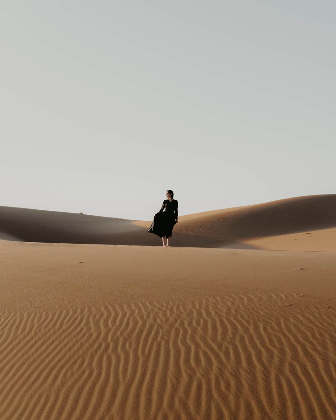 Sunset over rolling golden dunes at Six Senses Southern Dunes, casting burnt-orange light across the desert landscape