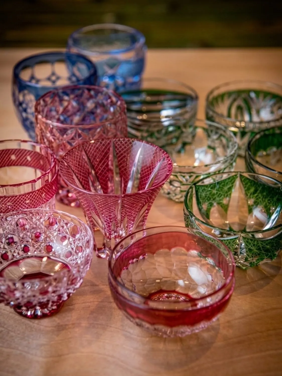 An artfully arranged collection of handcrafted Kiriko sake glasses in varying cuts and colours, displayed at the counter at Sushi Shikon, inviting diners to select their perfect vessel